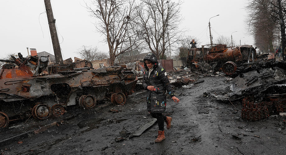 Une Ukrainienne marche devant des véhicules militaires russes dans l’une des zones reprises par l’armée ukrainienne dans la ville de Boutcha, en Ukraine, le 3 avril 2022. EPA-EFE/ATEF SAFADI