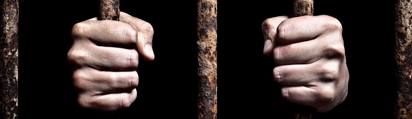 Hands on rusty cage bars. © Getty Images.