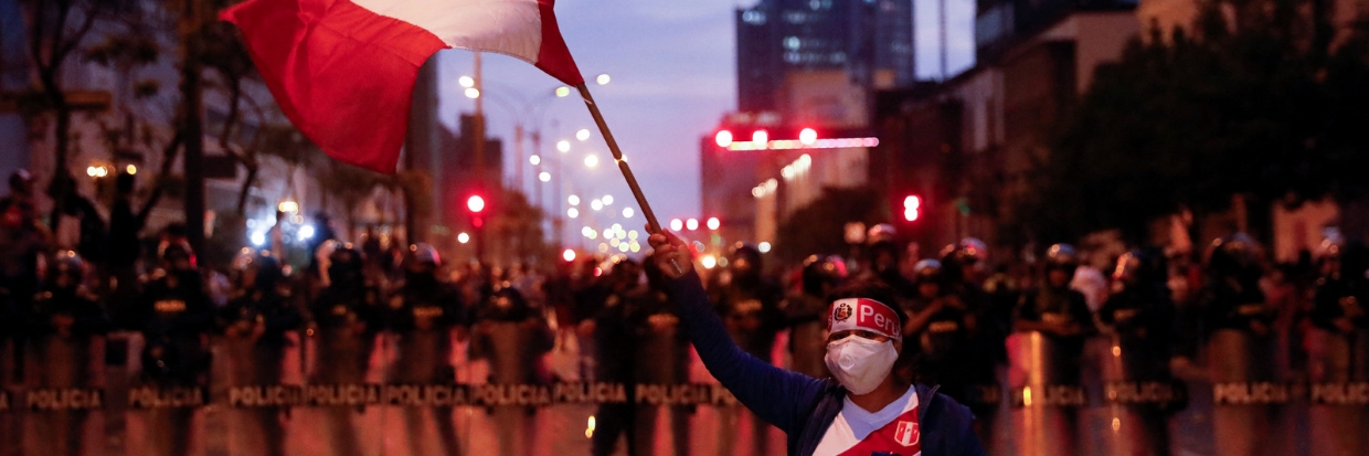 A protestor waves a Peruvian flag as police officers stand guard during a protest in Lima, Peru December 11, 2022. ©REUTERS / Alessandro Cinque