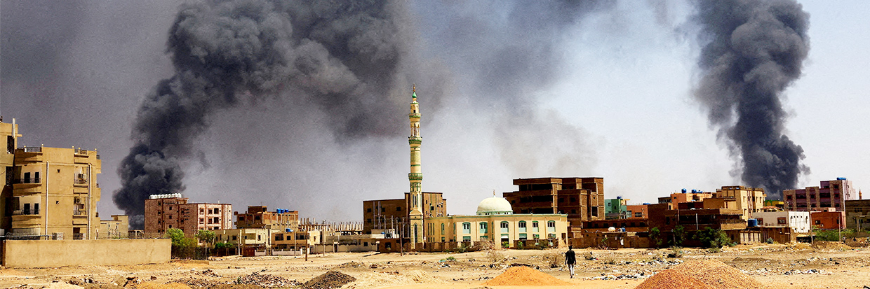 A man walks while smoke rises above buildings after aerial bombardments during clashes between the paramilitary Rapid Support Forces and the army in Khartoum North, Sudan, May 1, 2023 © REUTERS/Mohamed Nureldin Abdallah/File Photo