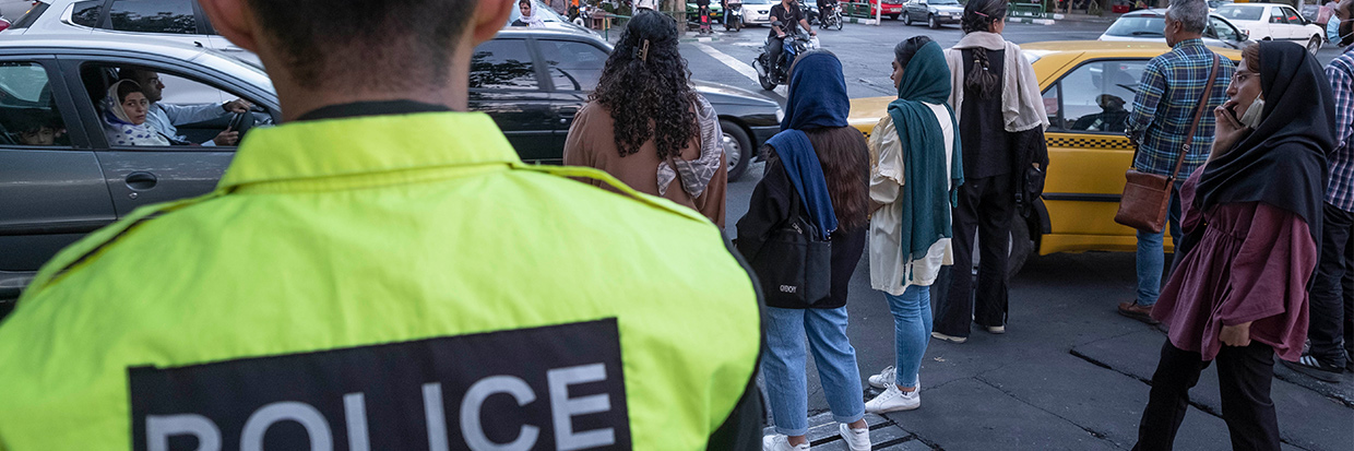 Irán : Varias mujeres esperan para cruzar la avenida Enghelab (Revolución) en el centro de Teherán a la vez que un miembro de la Fuerza Policial Especial de Irán vigila la zona, 12 de septiembre de 2023. © Morteza Nikoubazl/NurPhoto