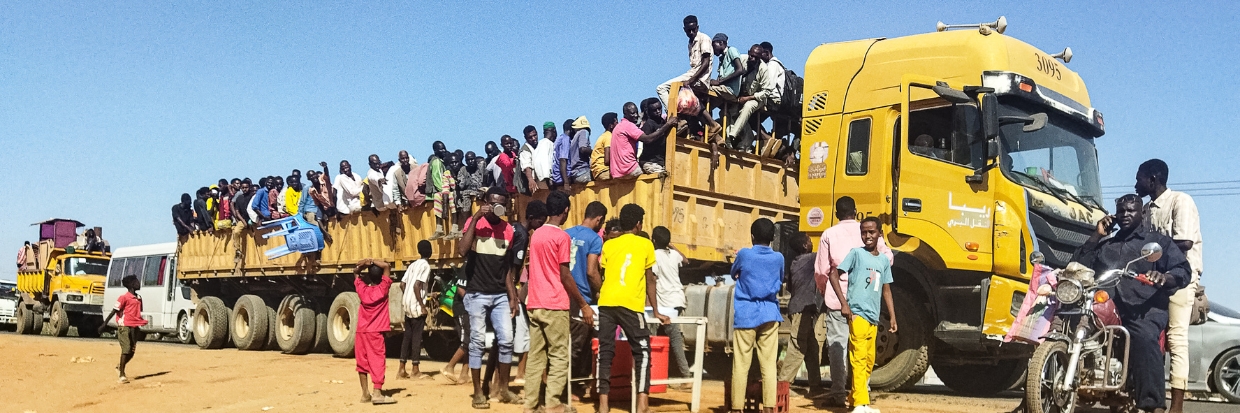 People displaced by the conflict in Sudan get on top of the back of a truck moving along a road in Wad Madani, the capital of al-Jazirah state, on December 16, 2023. Fighting between the Sudanese army and paramilitaries engulfed the aid hub of Wad Madani on December 15, triggering an exodus of civilians already displaced by eight months of war, an AFP correspondent reported. © AFP