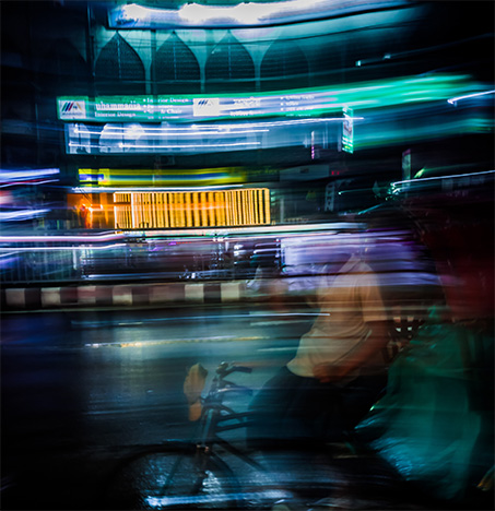 Un tirador de rickshaw espera pasajeros, en una noche lluviosa en una calle mojada. Foto de Syed Foyez Uddin en Unsplash (@genetx)