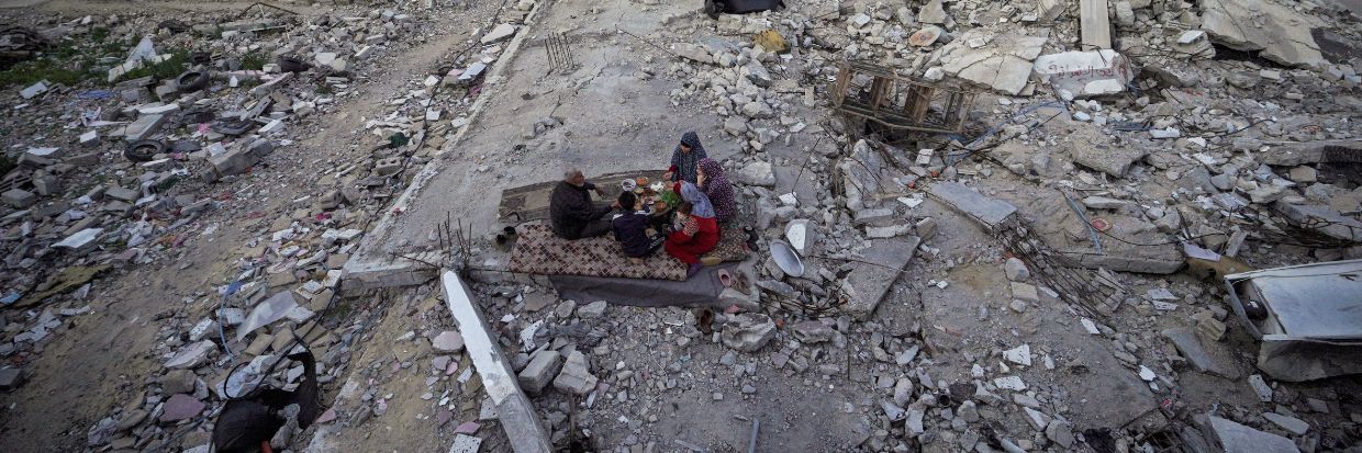 The Palestinian Al-Naji family eats an iftar meal, the breaking of fast, amidst the ruins of their family house, on the first day of the Muslim holy fasting month of Ramadan, in Deir el-Balah in the central Gaza Strip on March 11, 2024, amid ongoing battles between Israel and the militant group Hamas. (Photo by AFP)