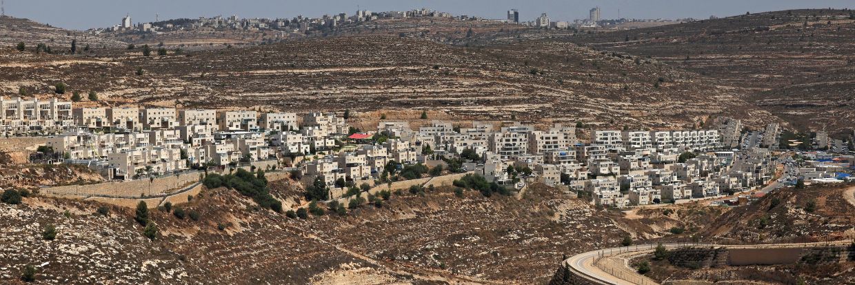 2023年9月8日，一条蜿蜒的道路在吉瓦特泽夫（Givat Zeev）的犹太人定居点（图中背景）和以色列占领的约旦河西岸城市拉姆安拉附近的巴勒斯坦村庄之间延伸。© AHMAD GHARABLI／法新社