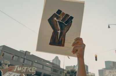 A woman in a crowd holds a demonstration sign depicting a balled fist, Charlotte, NC, USA, 3 June 2020 © Clay banks/UNSPLASH