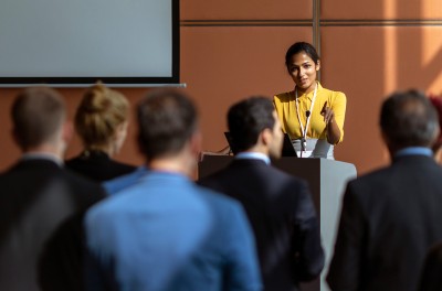 Smiling woman addresses a group from podium © Petra Debeljak/Getty Images