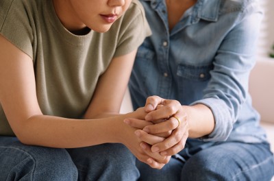 Two women sitting down and holding hands in a supportive stance.  © Getty Images/Chaytee