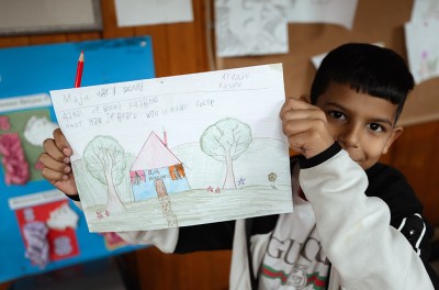 A young child from the Crvena Zvezda settlement shows a drawing he made, which features the Indigo community center, Serbia. © Stefan Vidojević from MaxNova Creative