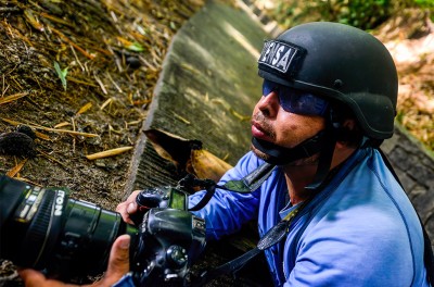 Journalist wearing a press helmet angles his camera. © Carlos Herrera