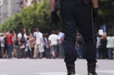 Two policemen stand behind a group of people protesting in the street. © Getty Images / Lalocracio