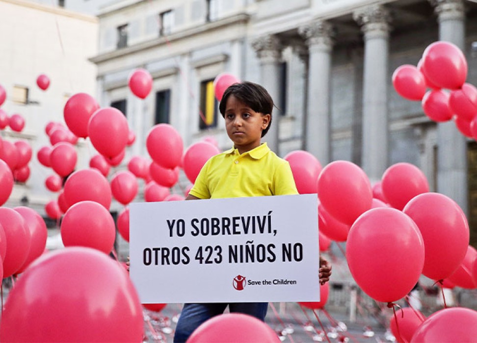 Eight-year-old Syrian refugee Zaid poses for photographers surrounded by balloons while holding a banner that reads, “I survived, 423 other children did not”, during an event organized by Save the Children in Madrid, Spain. EPA/EMILIO NARANJO