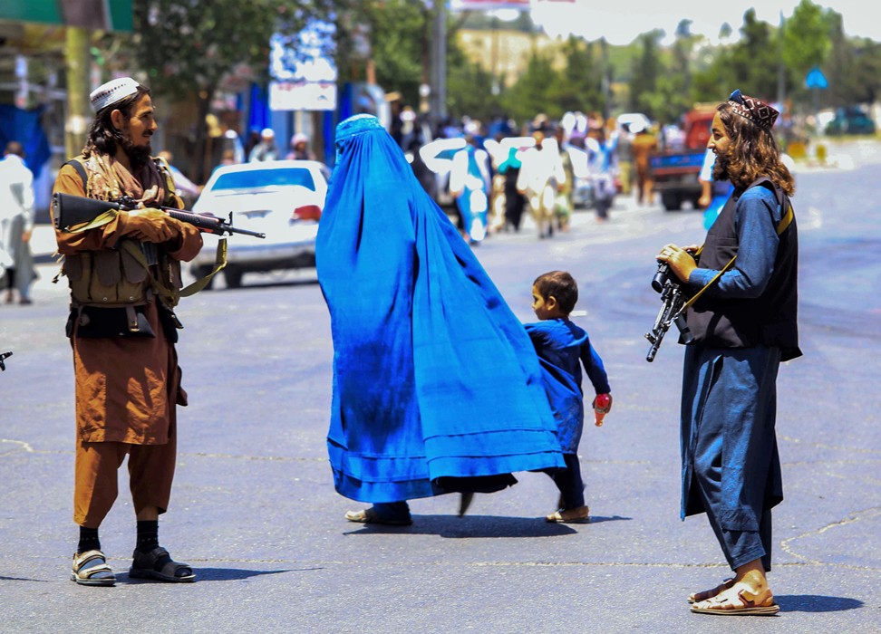 Afghan woman and child walking past Taliban soldiers © Credit – EPA-EFE