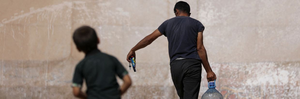 Un hombre lleva un contenedor de agua mientras pasa por delante de una tienda de campaña en un campamento para desplazados internos sirios, en el norte de Idlib, Siria, controlado por los rebeldes, el 25 de septiembre de 2022. © Reuters