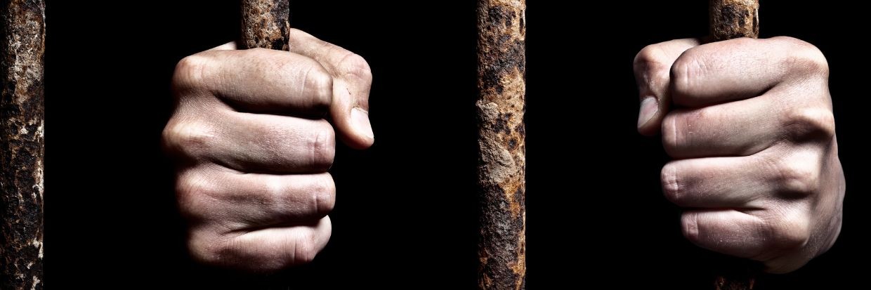 Hands on rusty cage bars. © Getty Images.