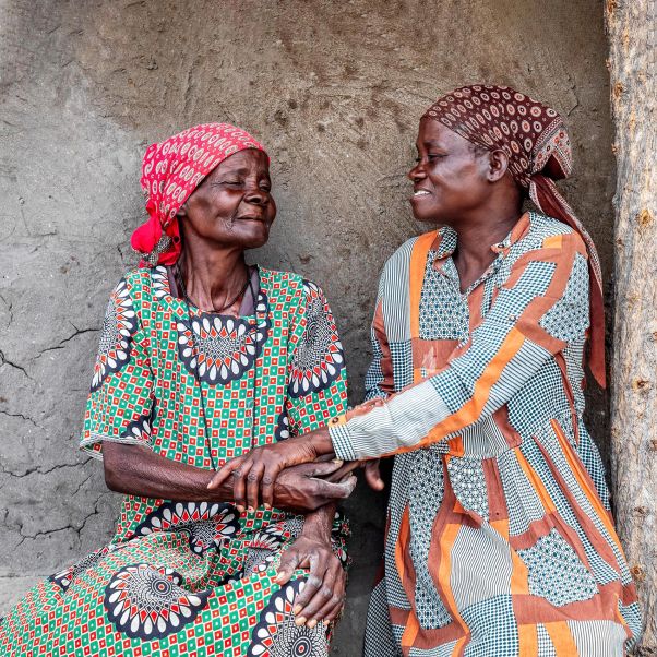 Two friendly elderly woman sitting next to the house wall in an African village - stock photo. © Getty Images