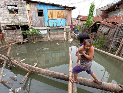 Une villageoise tenant un bébé traverse un pont improvisé dans une communauté touchée par le typhon Conson à Muntinlupa, dans le Grand Manille (Philippines) le 10 septembre 2021. © Francis R. Malasig/EPA-EFE