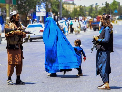 Afghan woman and child walking past Taliban soldiers © Credit – EPA-EFE