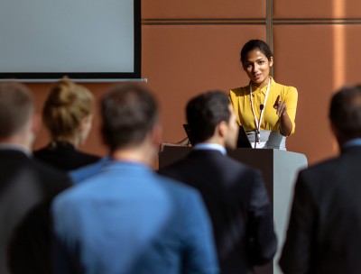 Smiling woman addresses a group from podium © Petra Debeljak/Getty Images