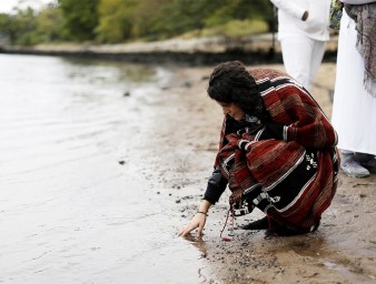 Indigenous woman touches water. © Credit – REUTERS