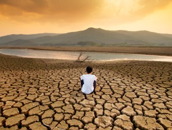 A child sitting on a drying lake underneath an orange-coloured polluted sky. ISTOCK / GETTY IMAGES PLUS