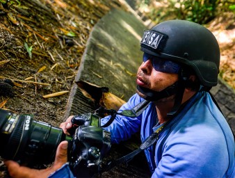 Journalist wearing a press helmet angles his camera. © Carlos Herrera