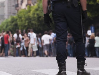 Two policemen stand behind a group of people protesting in the street. © Getty Images / Lalocracio