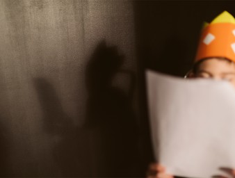 A child, whose face is hidden by a script he holds in his hands, during a theatre rehearsal. © Getty Images