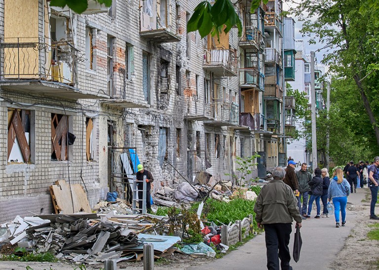 Locals walk past a residential building that was damaged during shelling in the outskirts of Kharkiv, Ukraine, 25 May 2022. © EPA-EFE/SERGEY KOZLOV