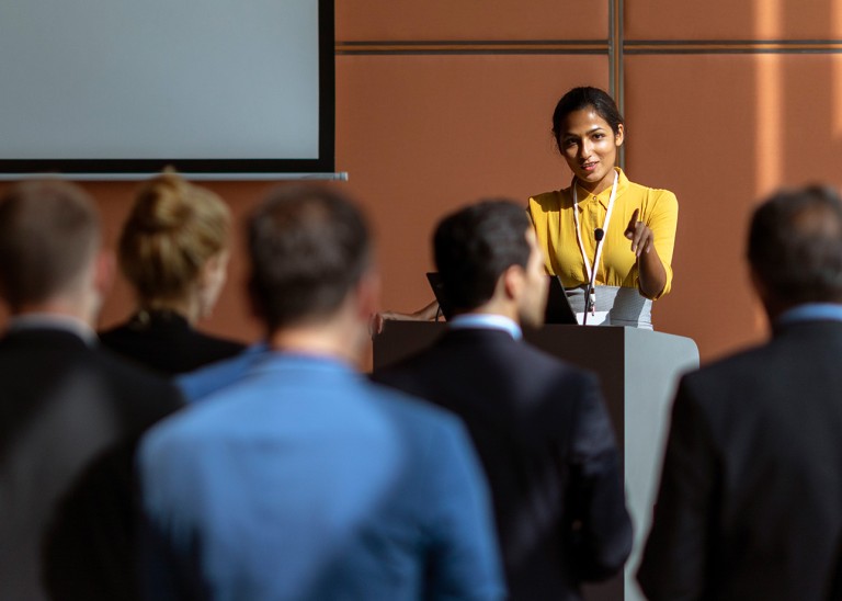 Smiling woman addresses a group from podium © Petra Debeljak/Getty Images