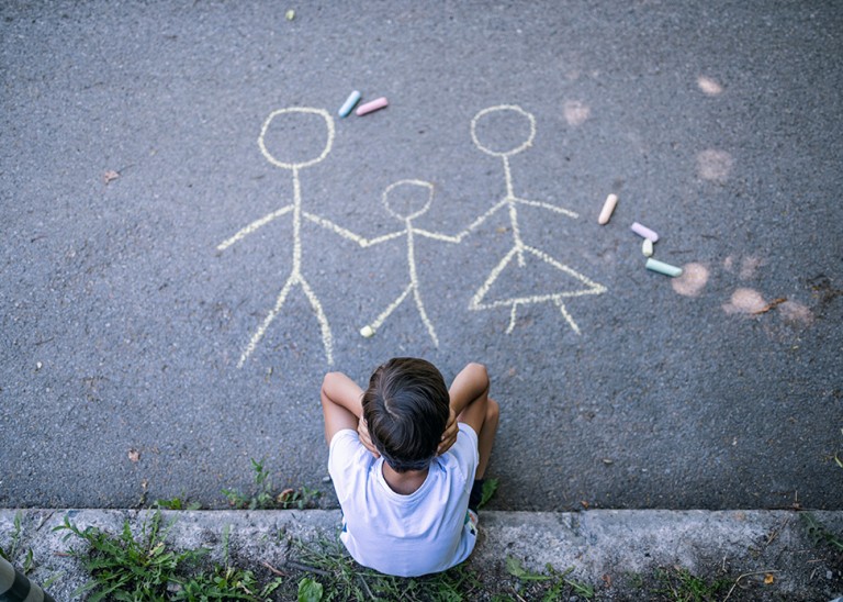 Overhead shot of little boy drawing a picture of his family and feeling sad. © Getty Images