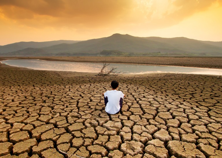 A child sitting on a drying lake underneath an orange-coloured polluted sky. ISTOCK / GETTY IMAGES PLUS