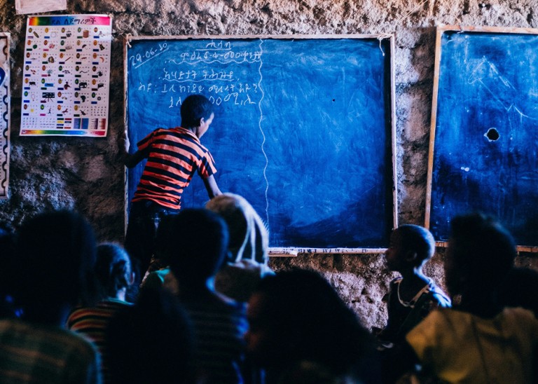 A schoolboy writes on a chalkboard in Ethiopia. © Betsy Arce