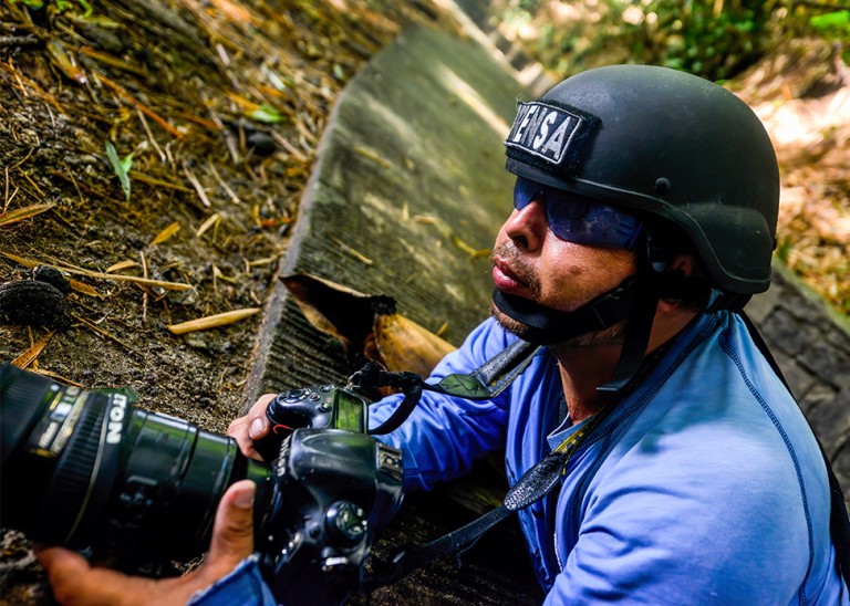 Journalist wearing a press helmet angles his camera. © Carlos Herrera